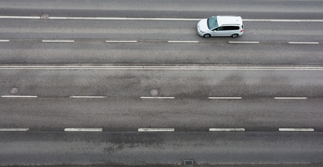 On the road with the asvalt cover, a white car is moving. view from above