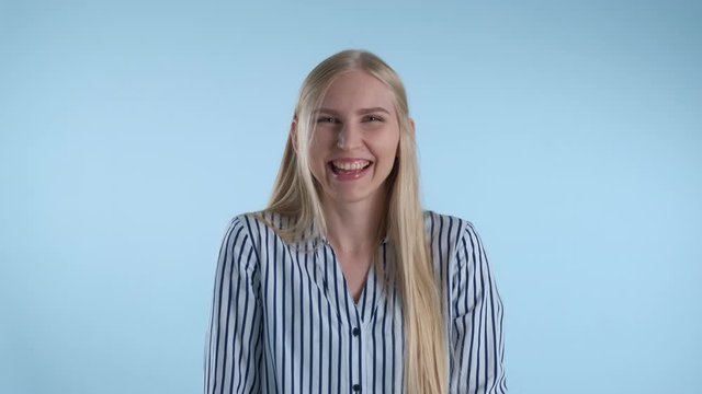 Happy young lady bursting in laughter on blue background. She has long blonde hair.