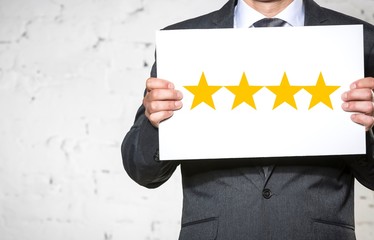 Midsection of smiling businessman holding four star rating placard while standing against white brick wall