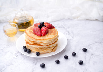 Stack of pancakes with topping, strawberry and blueberry.Placed in a white plate on a marble table and copy space.Eat with tea in the glass.
