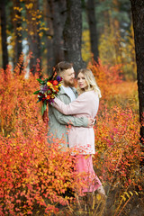 Couple in love walks through autumn forest. Hugs and kisses of men and women, relationships and love. Young couple stands in yellow red grass, a bouquet of flowers in girl hand