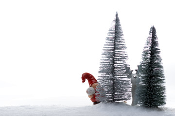 Stillleben bestehend aus Weihnachtsmannfigur aus Keramik mit Schneeball und Elch aus Pozellan zwischen Tannen und Schnee