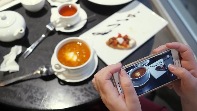 Woman takes pictures of food on the phone in a cafe, slow motion