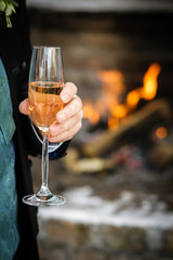 sektglas in hand vor dem kamin mit feuer