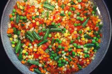 the vegetable mix  is fried in a pan on a black dark background