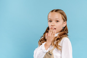 shocked and cute kid looking at camera and obscuring face isolated on blue