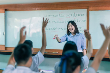 An Asian female teacher is teaching Japanese. The meaning of texts are "Mr. Suriya bought a shirt for the teacher, Mr Ittithep taught me Japanese, I have been taught Japanese from Mr Athithep".