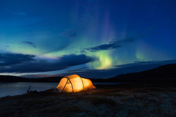 Northern lights dancing over an iluminated tent in Norway