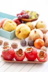 Fall fruits, like kakis,  close up over a wooden tray with a white wooden background with copy space.