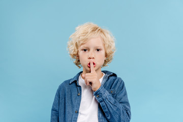 cute kid showing secret gesture and looking at camera isolated on blue - obrazy, fototapety, plakaty