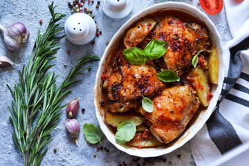 Baked chicken thighs with potatoes, tomato sauce and basil on a concrete background. View from...