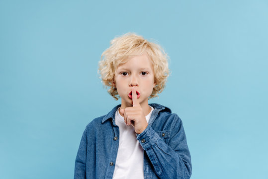 cute kid showing secret gesture and looking at camera isolated on blue