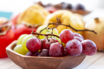 Naklejka na ściany i meble Fall fruits, like grapes, close up over a wooden bowl with a white wooden background with copy space.