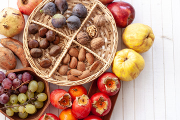 Top view to fall fruits on a wicker tray over a white wooden background with copy space.