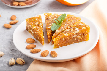 Traditional turkish candy cezerye made from caramelised melon, roasted walnuts, hazelnuts, cashew, pistachios on white ceramic plate and a cup of coffee on a gray concrete background. side view