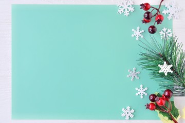 Christmas background with empty space for text, pine tree twig, beautiful white snowflakes and branch with red Christmas berries on mint paper backdrop. Winter card with elegant composition. New year 