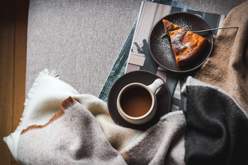 Slow weekend morning on a couch with coffee and a piece of cake. Dark mood flatlay