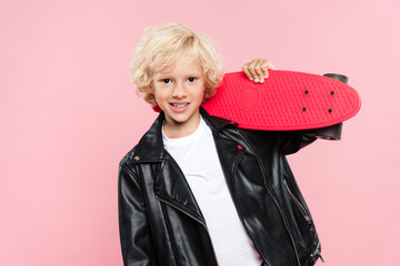 smiling and cute kid holding penny board isolated on pink