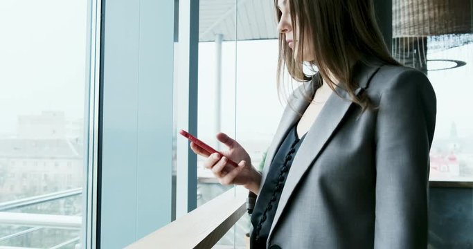 Portrait of young attractive woman looking at smartphone on the office near bif window