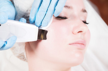 Close-up face of an attractive adult girl in a spa beauty salon at a reception by a professional cosmetologist for ultrasound cleaning of the face