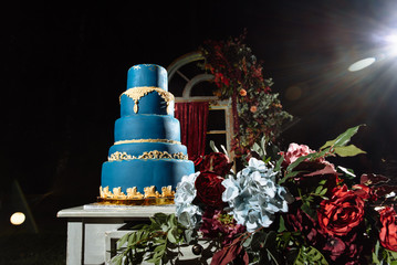 Big luxurious wedding cake in blue and gold colors, outdoors near the festive arch, in the evening