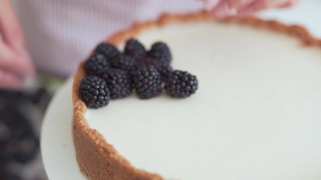 Close-up scene of a cook who has just made a cheesecake and now has decorating it with berries : blackberries and bilberries.