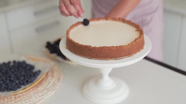 Close-up scene of a cook who has just made a cheesecake and now has decorating it with berries : blackberries and bilberries.