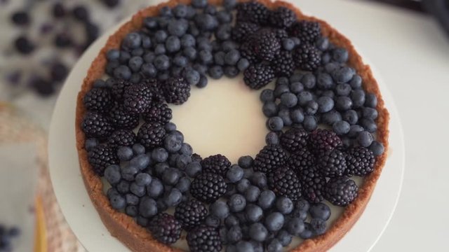 Close-up scene of a cook in a black gloves who has just made a cheesecake and now has decorating it with berries : blackberries and bilberries.
