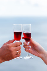 Glasses with red wine in hands on a background of the sea.