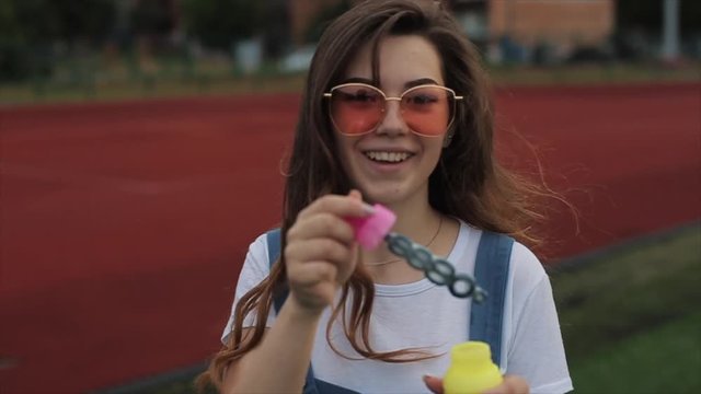 Beautiful young woman in sunglasses blowing soap bubbles outdoors and spinning around. Close view. Slow motion. girl in trendy orange sunglasses