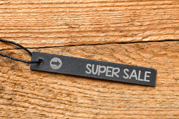 Super Sale text on black tag and wooden background. Sale time in stores - high resolution photo.