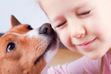 A dog sniffs a little girl's face.