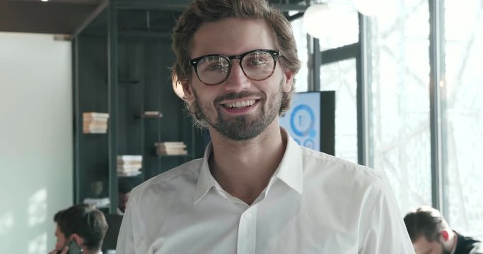 Portrait of Attractive Businessman Wearing Eyeglasses Standing in Front of Camera. Posing on Camera objective. Looking Happy and Smiling Sincerly. Handsome Successful Businessman Indoor Office.