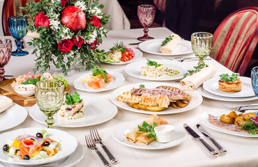 Served for holiday banquet restaurant table with dishes, snack, salads, cutlery, wine and water glasses. European food in a restaurant setting. Table set for an event party. catering