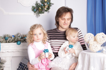 father with two daughters are sitting at a table in a room with New Year's decorations