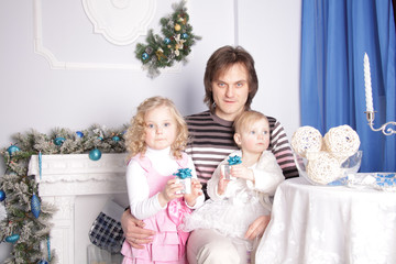 father with two daughters are sitting at a table in a room with New Year's decorations