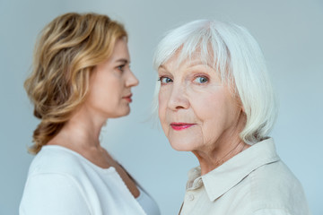 selective focus of mother looking at camera and daughter on background isolated on grey