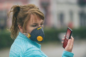 Woman wearing a real anti-smog face mask and checking current air pollution with smart phone app