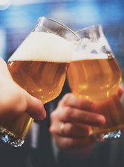 Close-up view of a two glass of beer in hand. Beer glasses clinking in bar or pub