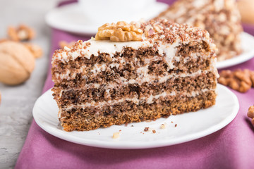 Homemade cake with milk cream and walnuts with cup of coffee on a gray concrete background, side view, selective focus.