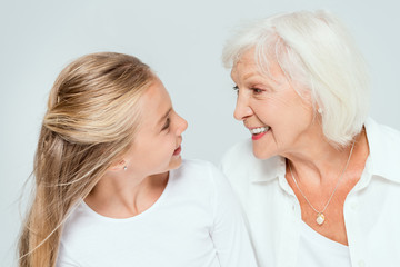 smiling granddaughter and grandmother looking at each other isolated on grey