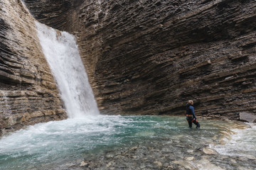 lonely woman with canyoning costume and a red helmet in her hand in the foreground inside the turquoise water in a waterfall of a mountain canyon