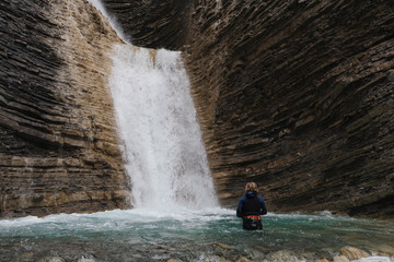 woman in canyoning costume in turquoise water submerged to the waist of a waterfall in a mountain canyon