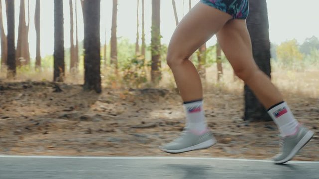 Girl in sportswear jogging in the forest, only legs closeup. Girl runs along the road in a pine forest, slow-motion 4k video. Female jogging outdoors. US flag printed on the socks