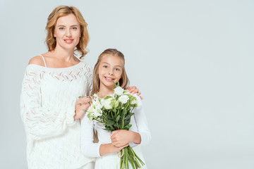 attractive mother hugging smiling daughter with bouquet isolated on grey