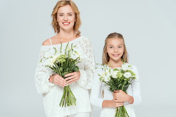 attractive mother and smiling daughter holding bouquets isolated on grey