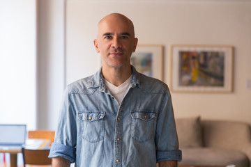 Front view of handsome serious bald man posing at home. Middle aged man wearing casual, looking at camera. Male portrait concept