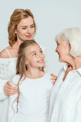 smiling granddaughter, mother and grandmother looking at each other isolated on grey