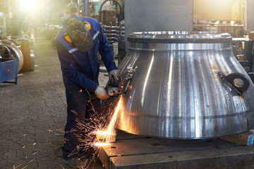 A worker processes a weld on a large valve