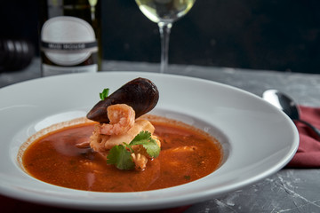Fresh seafood soup in a white plate on dark background, side view
